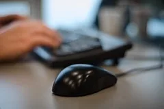 Hands typing at a keyboard and mouse on an office desk