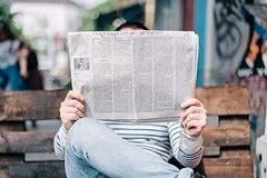 A person reading a large open newspaper